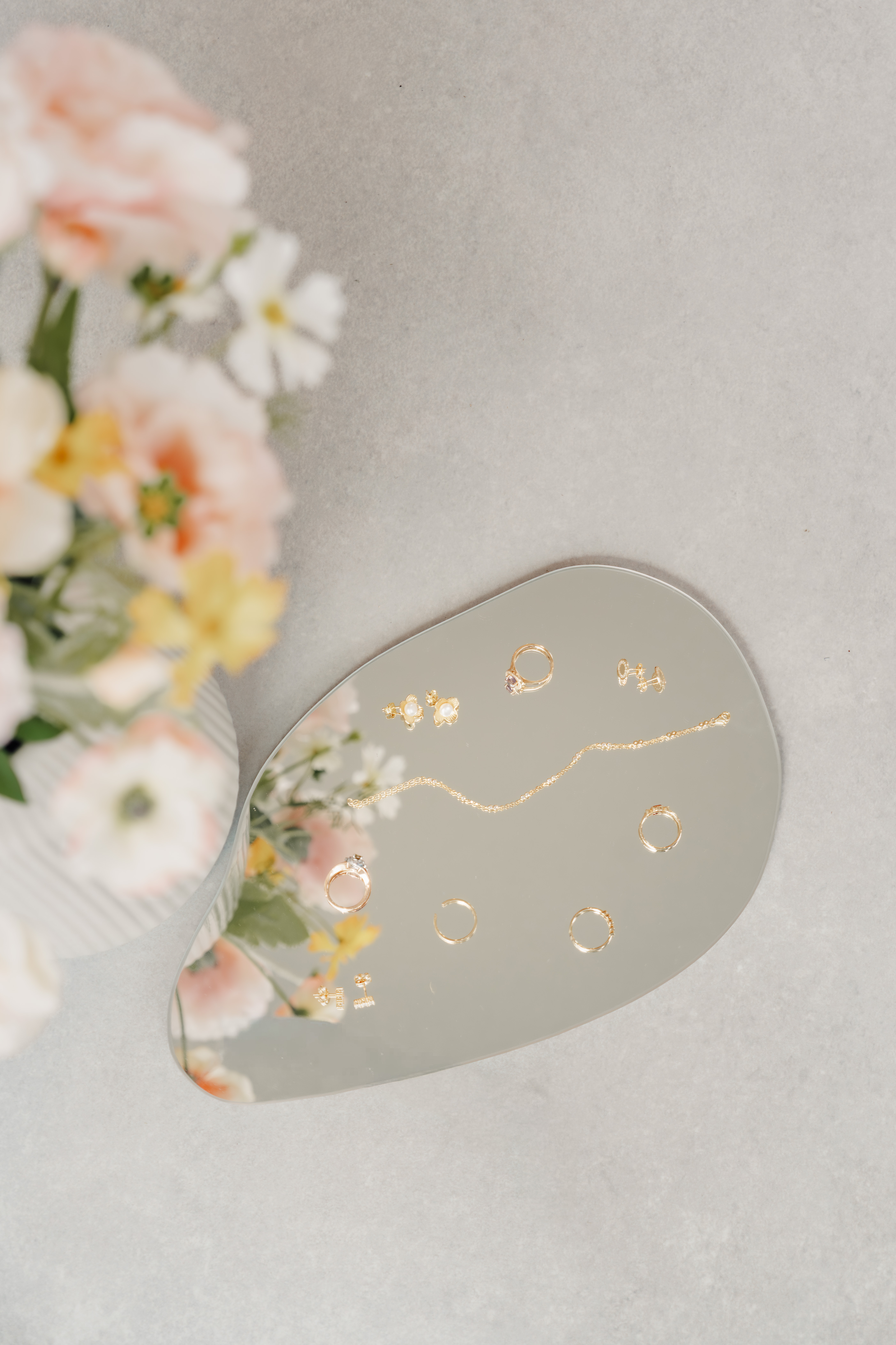 Gouden juwelen op een spiegel naast een boeket veldbloemen in zacht zonlicht